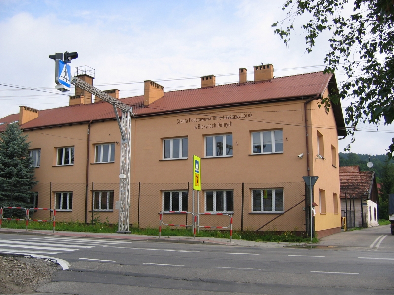 Budynek Szkoły Podstawowej w Biczycach Dolnych, pomarańczowy jednopiętrowy budynek z czerwonym dachem, przed budynkiem ulica z przejściam dla pieszych