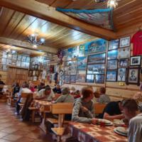 Wnętrze restauracji, przy stołach kilkanaście osób, sufit i ściany drewniane, na ścianie duża ilość zdjęć i obrazów w ramkach