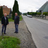 Wójt gminy Bernard Stawiarski i Starosta Powiatu Nowosądeckiego stoją obok siebie na drodze, wójt ma uniesioną rękę, w tle droga i budynki mieszkalne