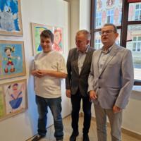 Wójt gminy oraz dyrektor Szkoły podstawowej w Chełmcu z dziećmi w tle na ścianach wystawione prace konkursowe