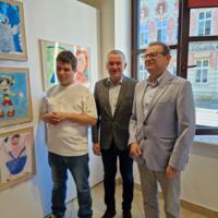 Wójt gminy oraz dyrektor Szkoły podstawowej w Chełmcu z dziećmi w tle na ścianach wystawione prace konkursowe