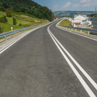 Zdjęcie dwupasmowej asfaltowej drogi, po lewej stronie niewielki zielony pagórek