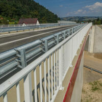 Zdjęcie mostu drogowego biegnącego nad inną drogą - po obu stronach barierki w tle góry
