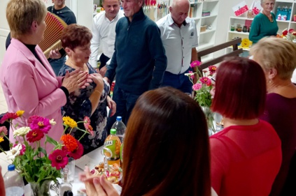 Spotkanie sołeckie - ok 10 osób na świetlicy przy stole zastawionym poczęstunkiem napojami i ozdobionym kwiatami, jedna osoba trzyma w rękach harmonię